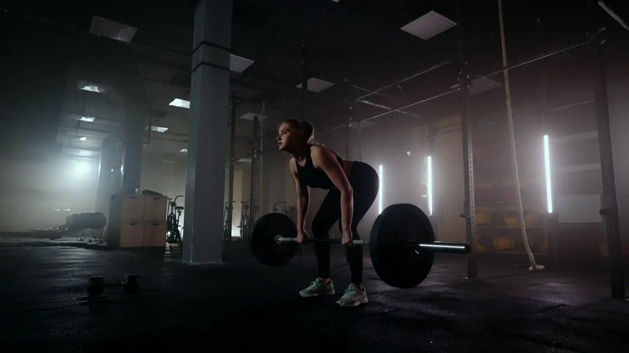 Slow motion A woman lifts a barbell in a dark gym with a lot of weight A strong young woman lifts weights for a workout