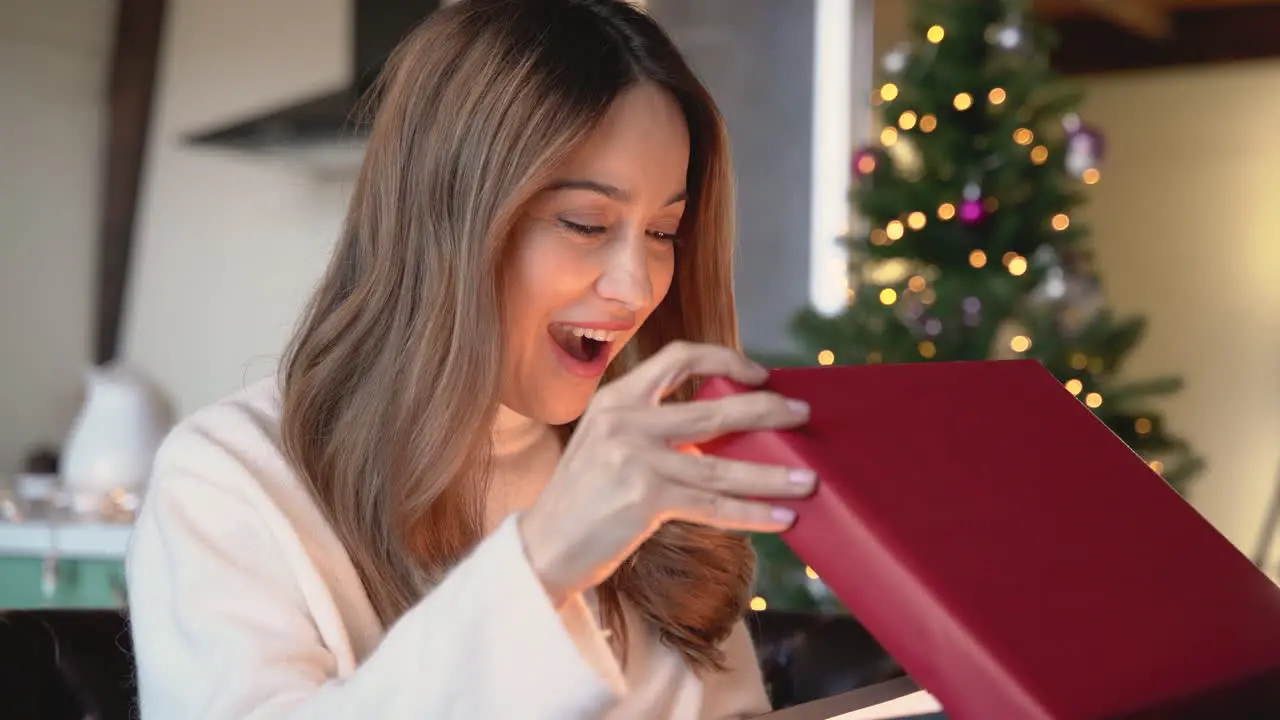 Happy Woman Opens A Christmas Present In A Living Room With Christmas Decorations