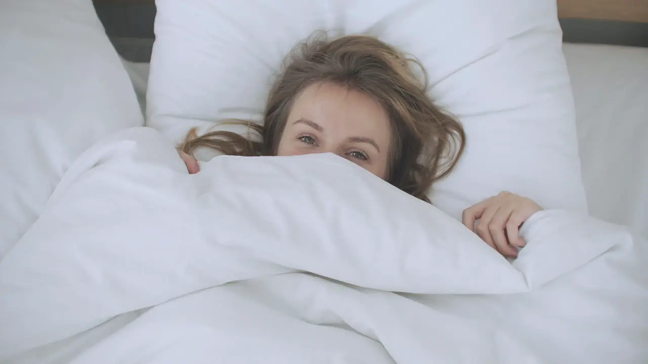 Happy Woman peeking out from her blanket in bed and Smiling Peeking under duvet and smiling