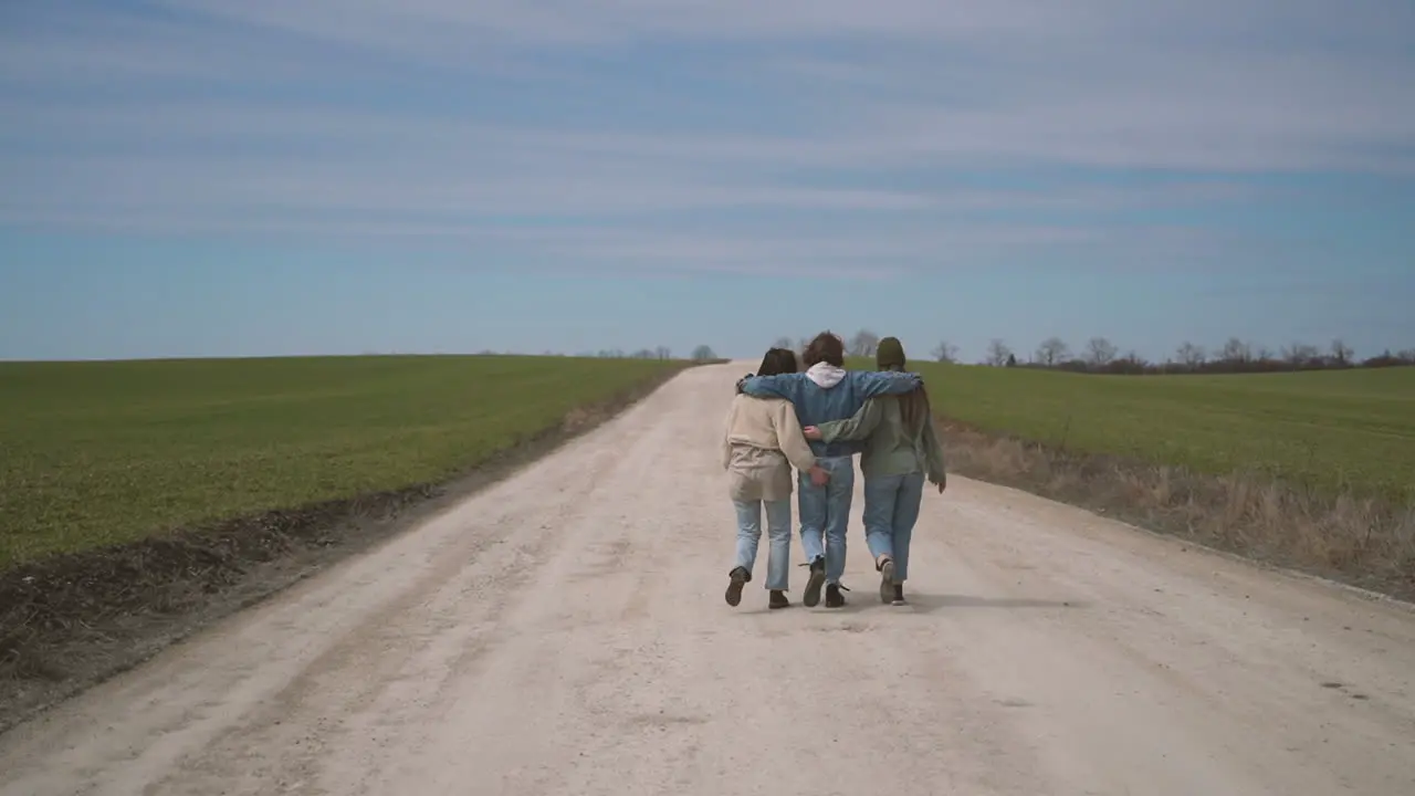 Two Young Girls And A Young Boy Walk Backwards Along A Road In Each Other's Arms