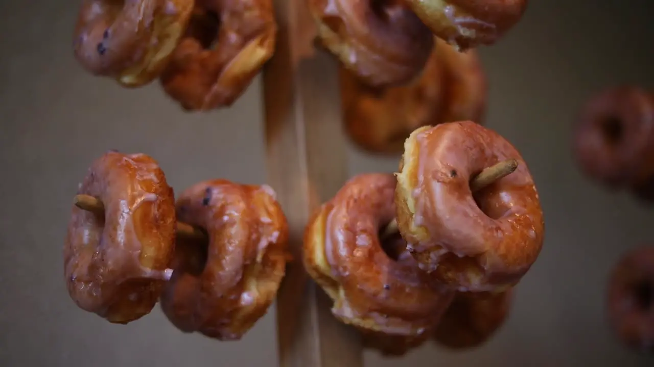 Slow panning shot of dozens of glazed donuts hanging on multiple donut racks