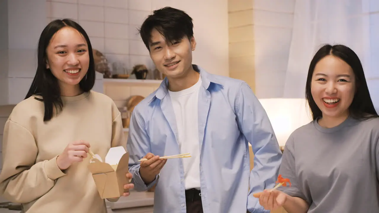 Three Japanese Friends Eating Japanse Food Around The Kitchen Counter Then They Look At Camera And Smile