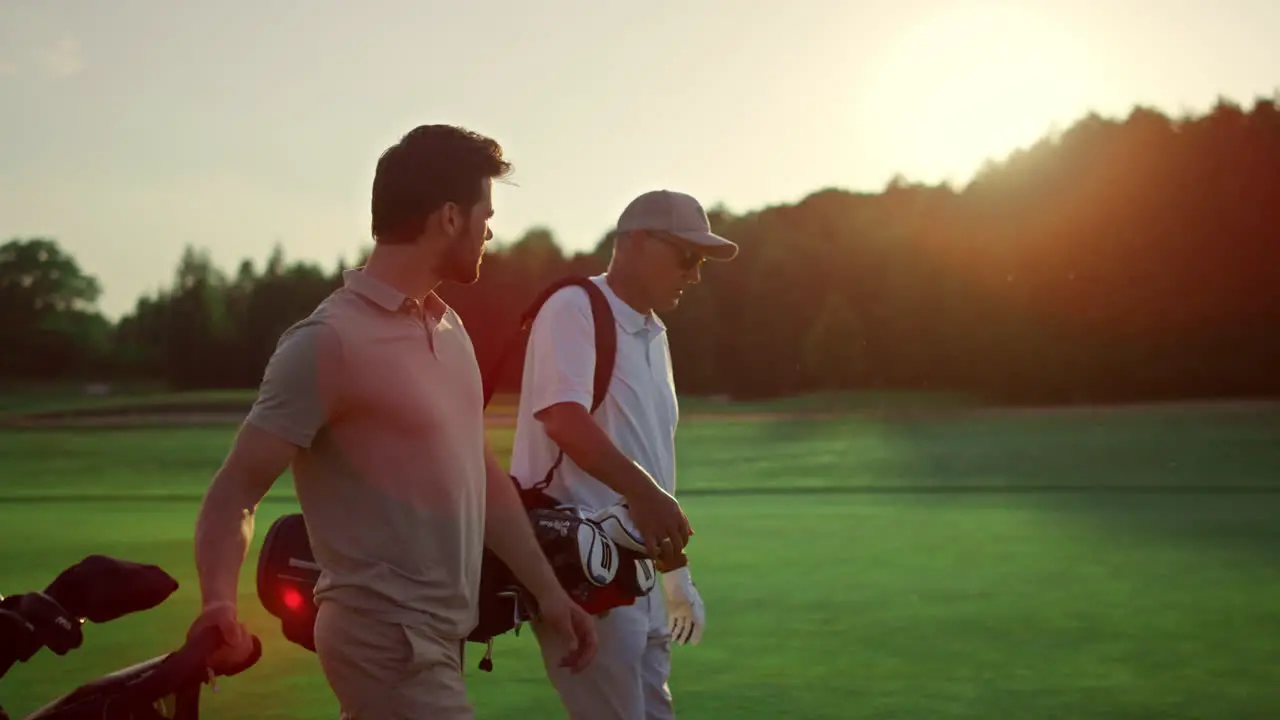 Businessmen walking golf course outside Two players carry clubs in sportswear