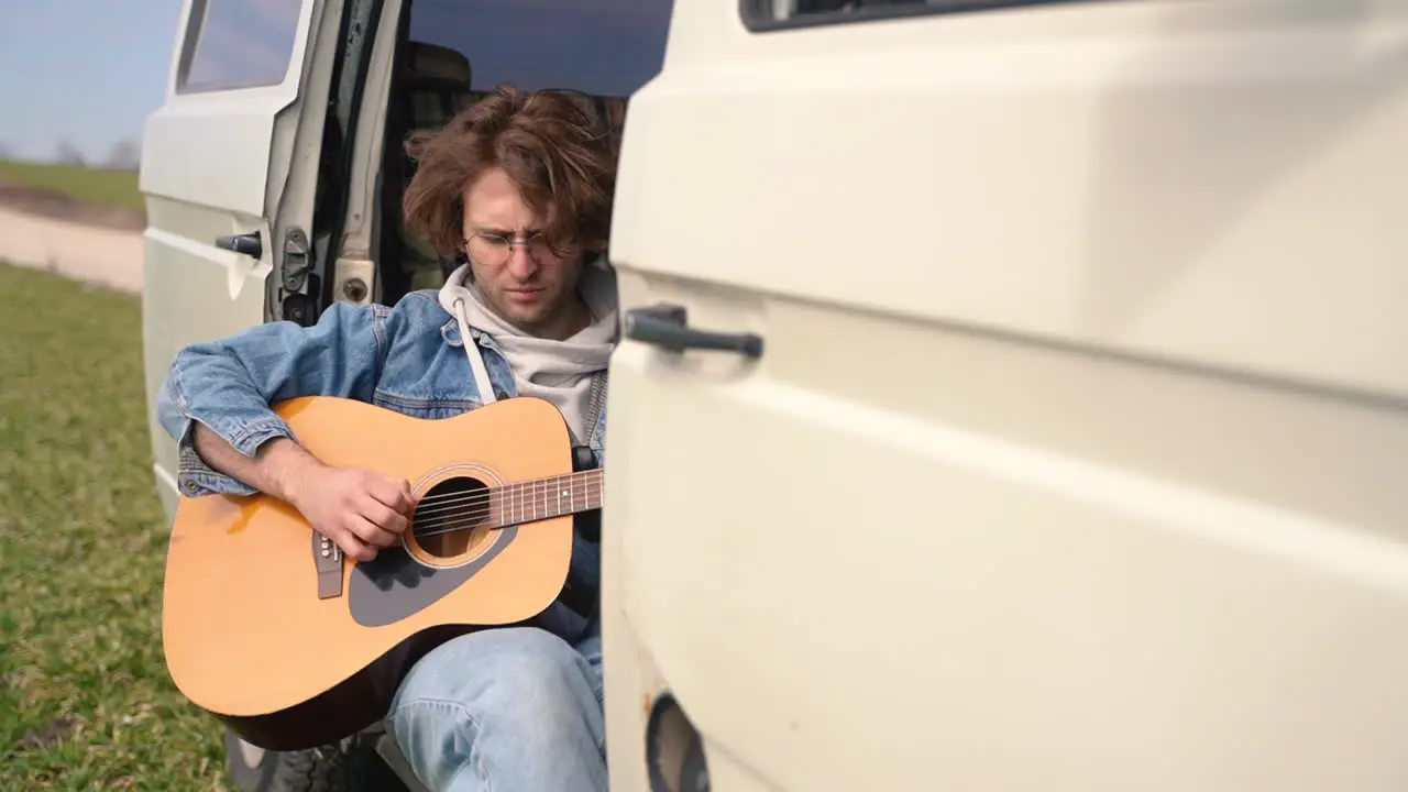 A Young Guy With Glasses Plays The Guitar In The Back Of A Caravan