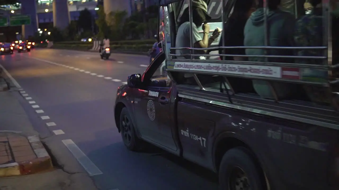 A public Songthaew taxi bus with locals is slowly passing by on a street in Bangkok during nighttime