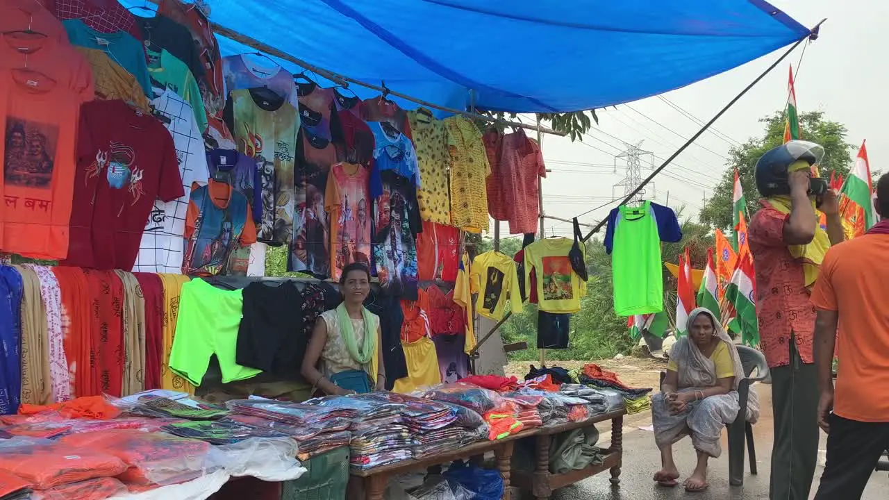 A lady shopkeeper sitting at a makeshift shop that sales clothes with lord shiva prints to pilgrims going to Kanwar Yatra