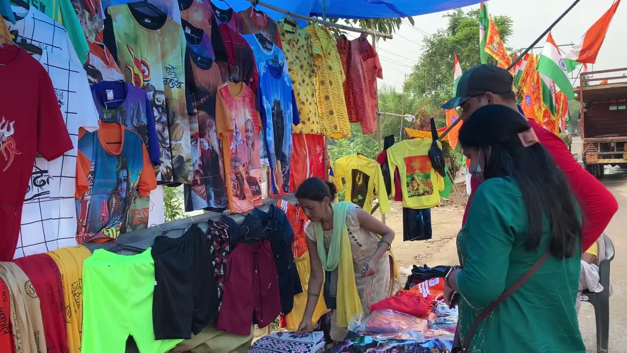 A lady shopkeeper taking down clothes with lord shiva prints for sale to pilgrims