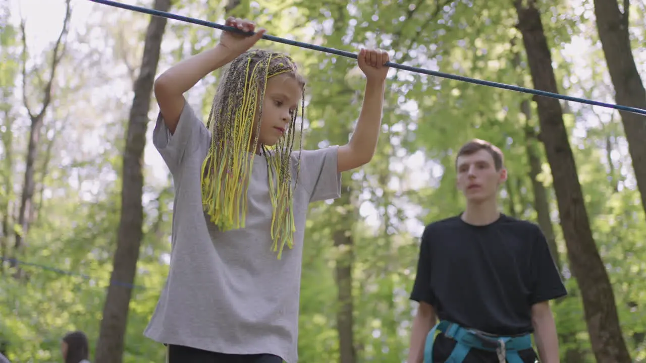 Active child fearlessly climbs the ropes between the trees Girl in an adventure park are pass obstacles on the rope road children camp summer camp