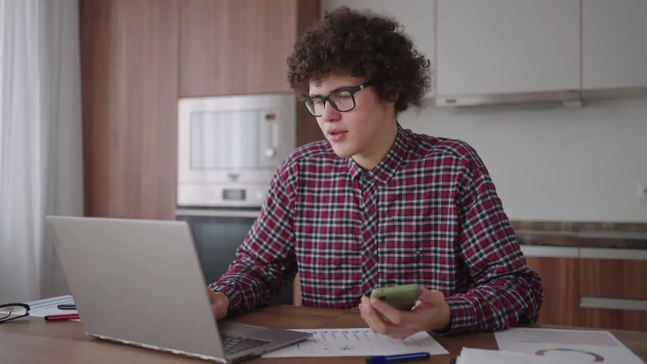 Young man with smartphone in his hands Modern businessman or student at home office Freelancer at work Young student man study at home with laptop and uses a smartphone