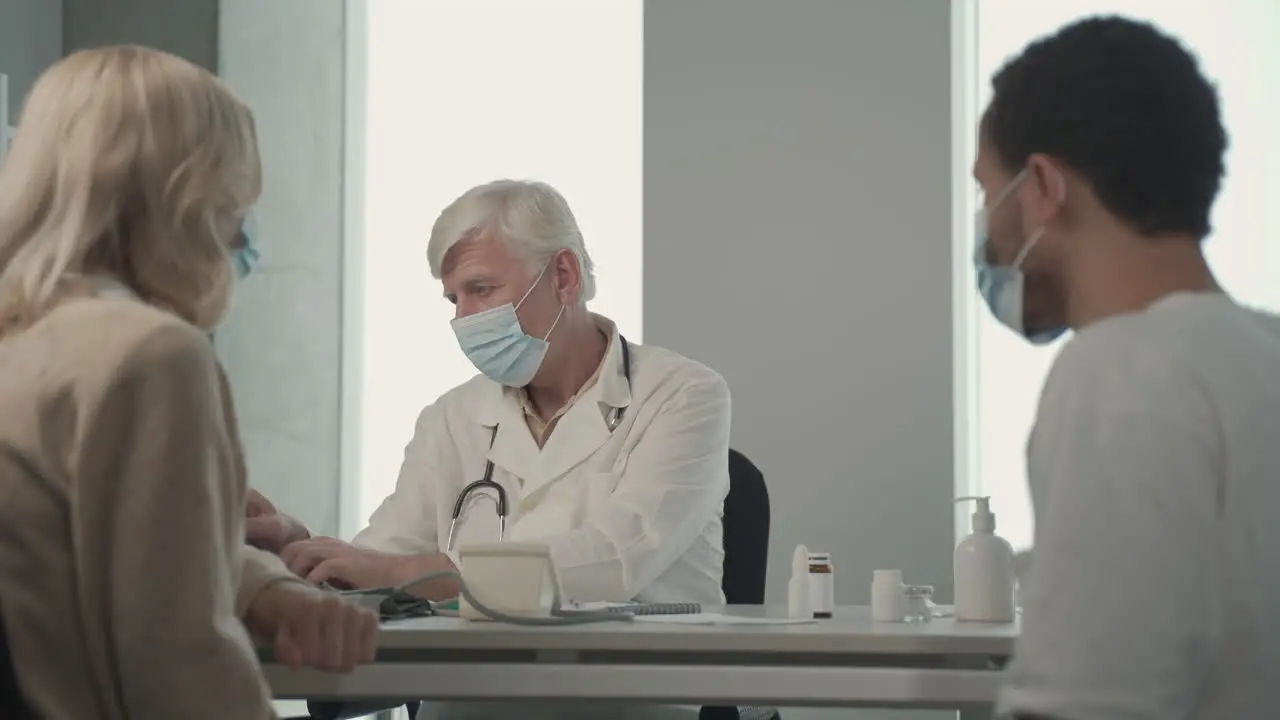 A Grey Haired Middle Aged Doctor In A Facemask Asking Questions To A Young Black Man