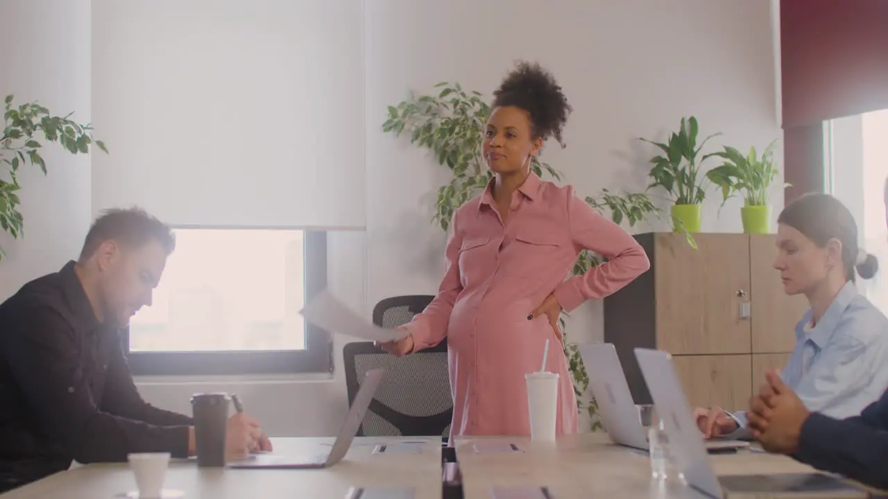 Pregnant Woman Finishing Explaining A Project In Front Of Her Coworkers In A Meeting Room