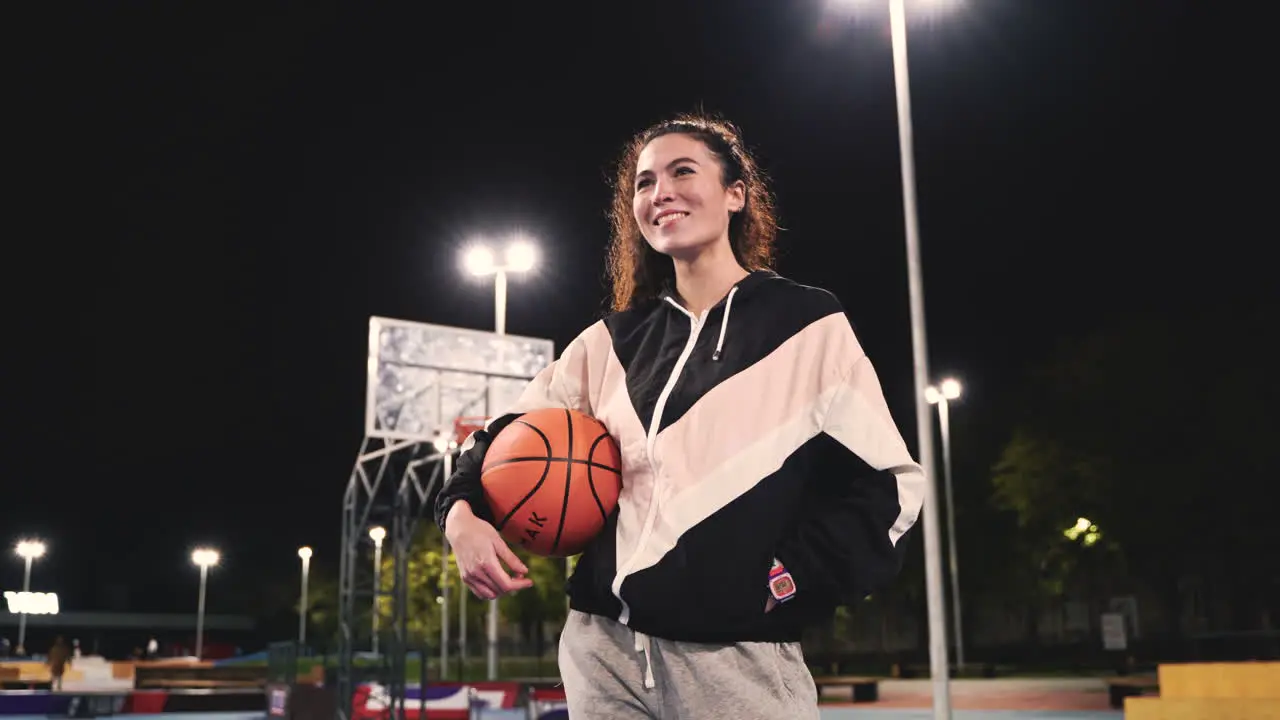 Beautiful Female Basketball Player Holding Ball And Smiling At Camera On Outdoor Court At Night