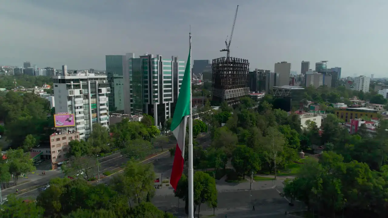 Orbital footage left to right around mexican flag with view of an principle avenue in Mexico City at morning