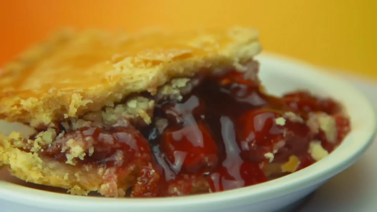 [Camera Used Canon C300] Close-up a rotating cherry pie slice with golden crust and oozing cherries