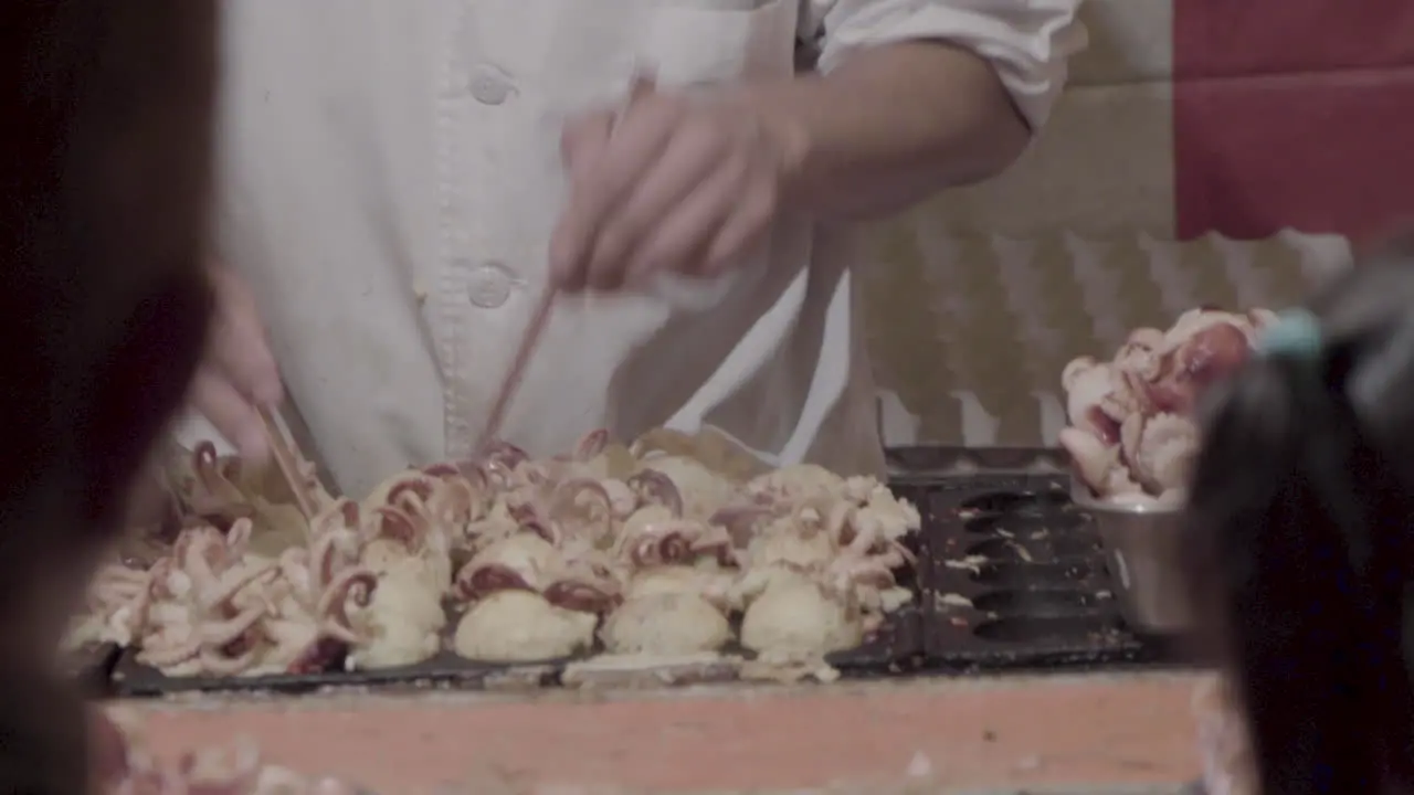 Professional male cook is preparing japanese food called Takoyaki with chopsticks pretty fast