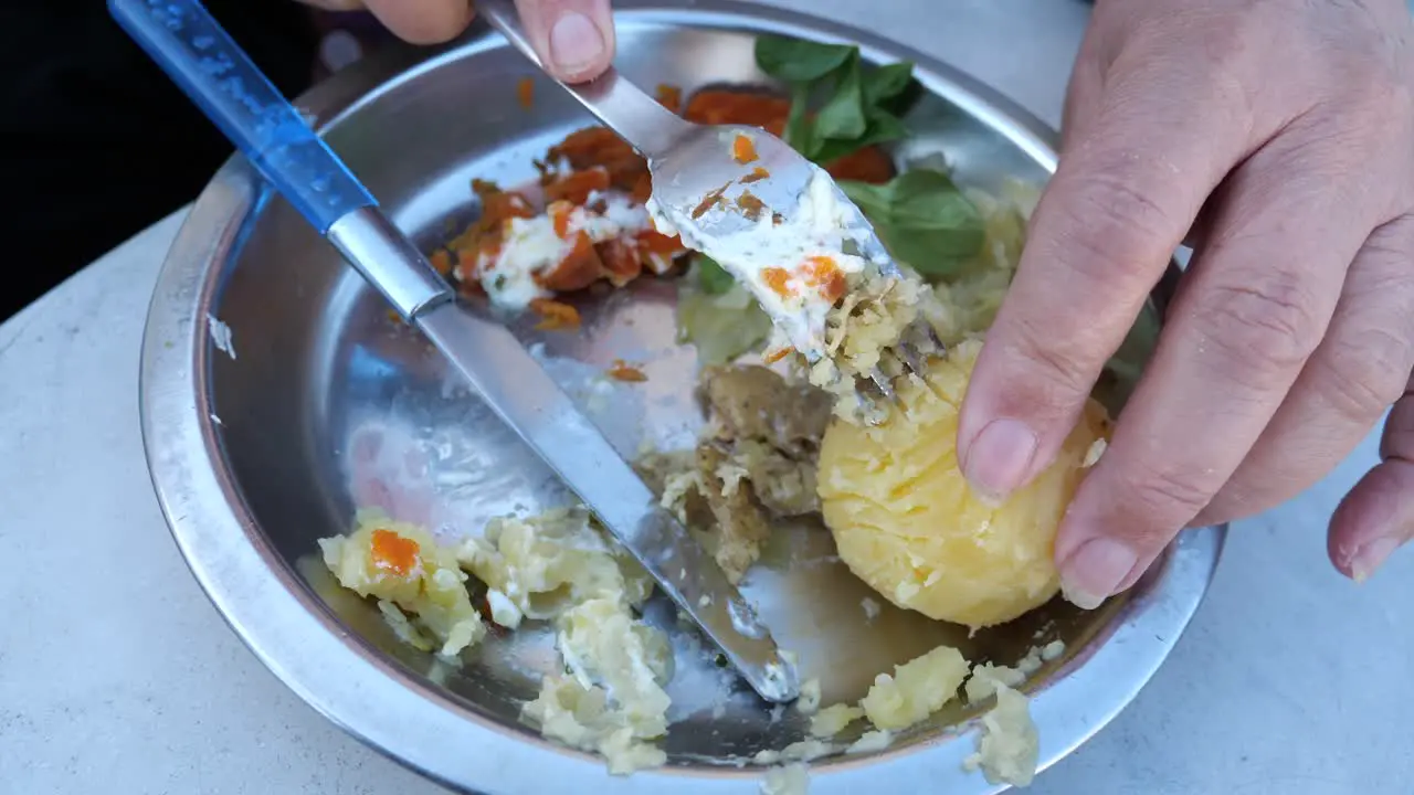 Elderly female hand peeling boiled potato with fork then mashes it and mixes it with mashed carots