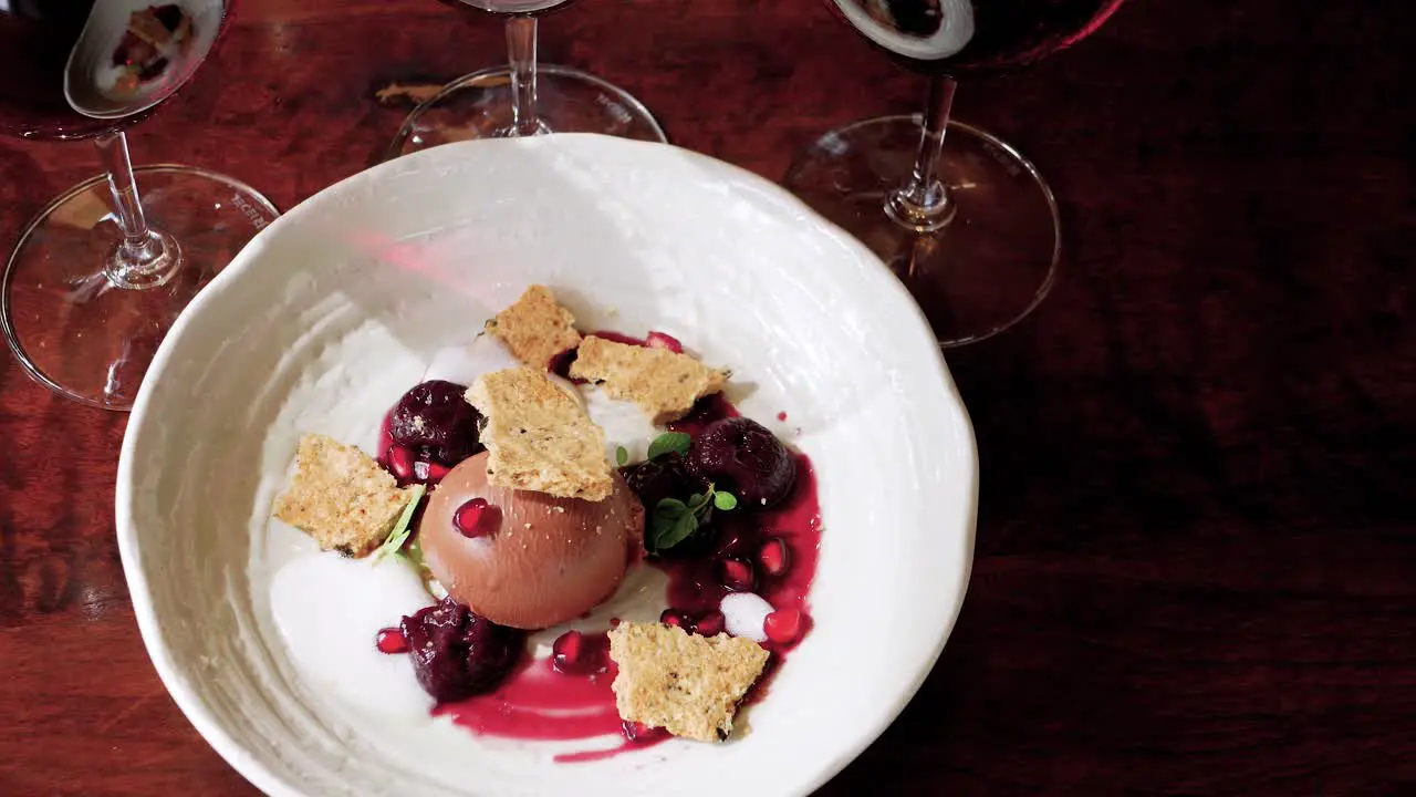 Fine dining dessert of Milk Chocolate Crémeux with Star Anise Cherries Black Olive Shortbread Pomegranate Marjoram and Liquorice Foam