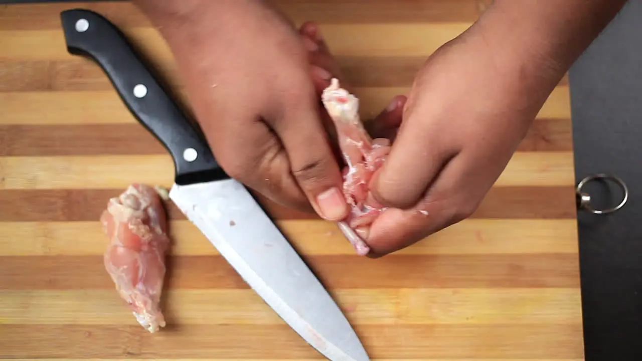 men cutting fresh chicken wings with a sharp knife and shaping into a lollipop on a chopping board preparing for food