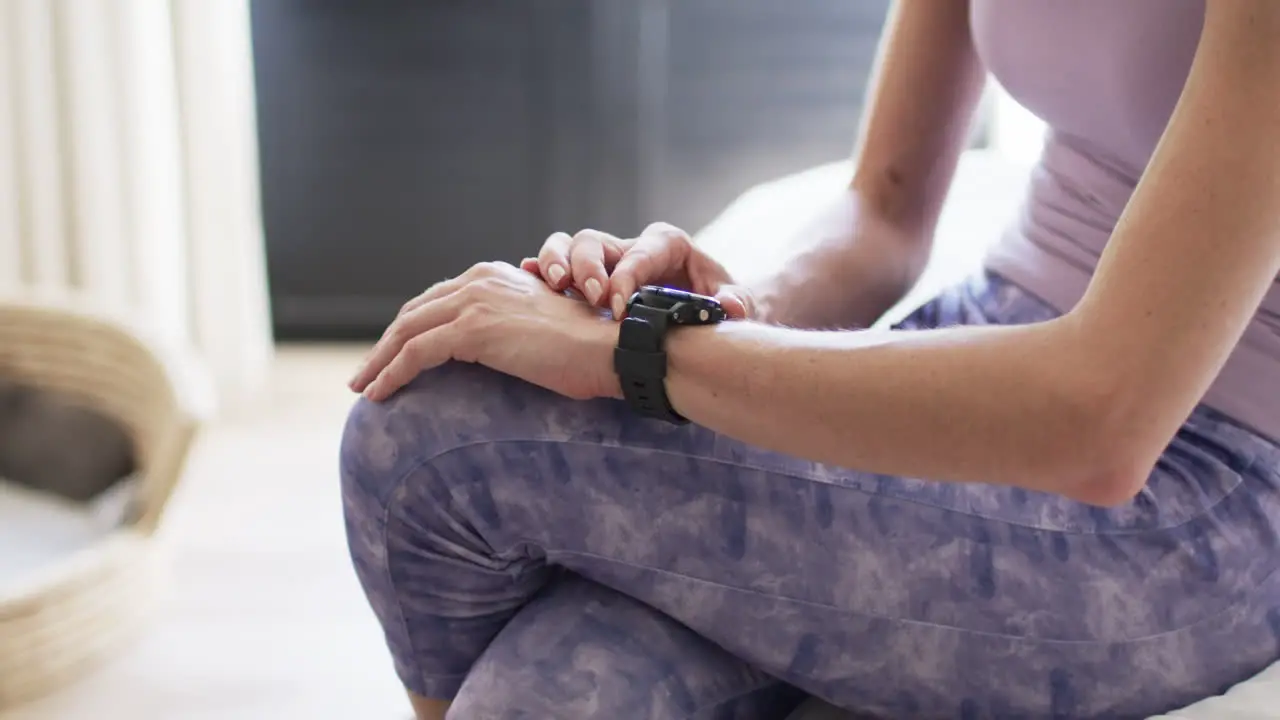 Middle-aged Caucasian woman checks her smartwatch at home with copy space