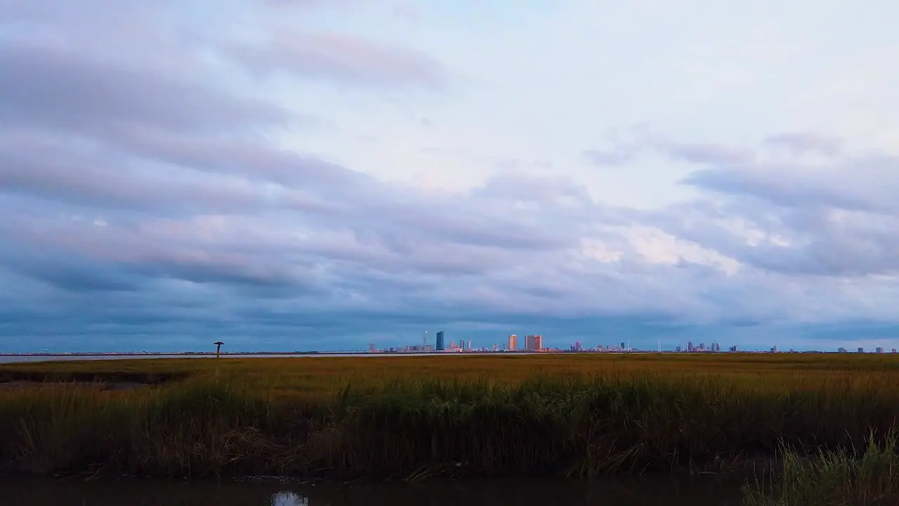 HD MOTIONLAPSE Zoom in from left to center Atlantic City skyline in distance over waterway with mostly cloudy sky day to night with clouds turning pink purple and blue