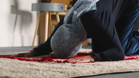 Muslim Woman Wearing Hijab At Home Kneeling On Prayer Mat And Praying