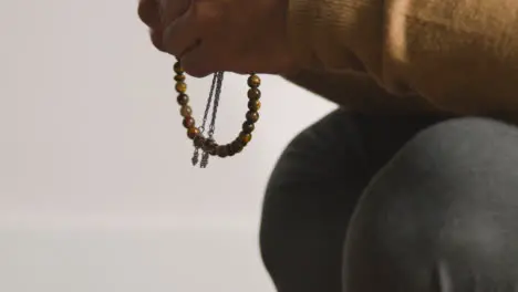 Close Up Of Muslim Man Praying Holding Prayer Beads Against White Background