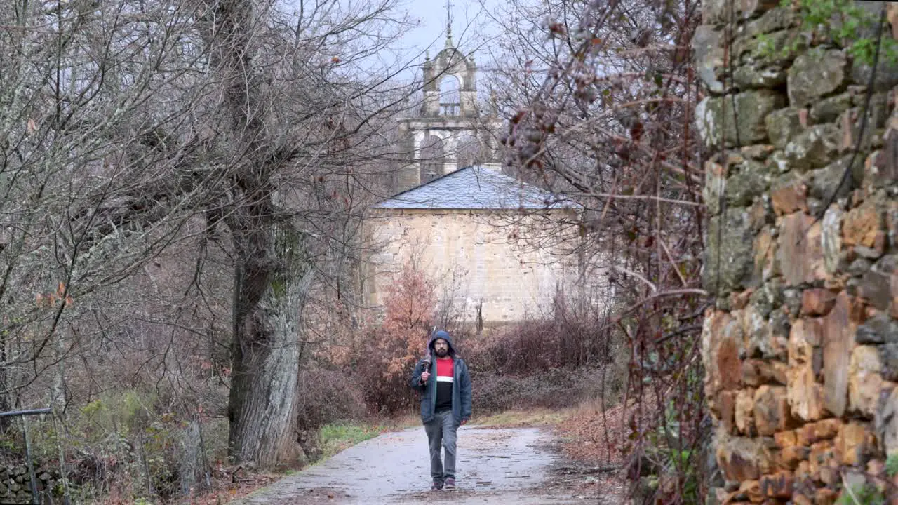 Young man walks out of a rural church in the middle of the nature after a rainy day with a close umbrella on his hand