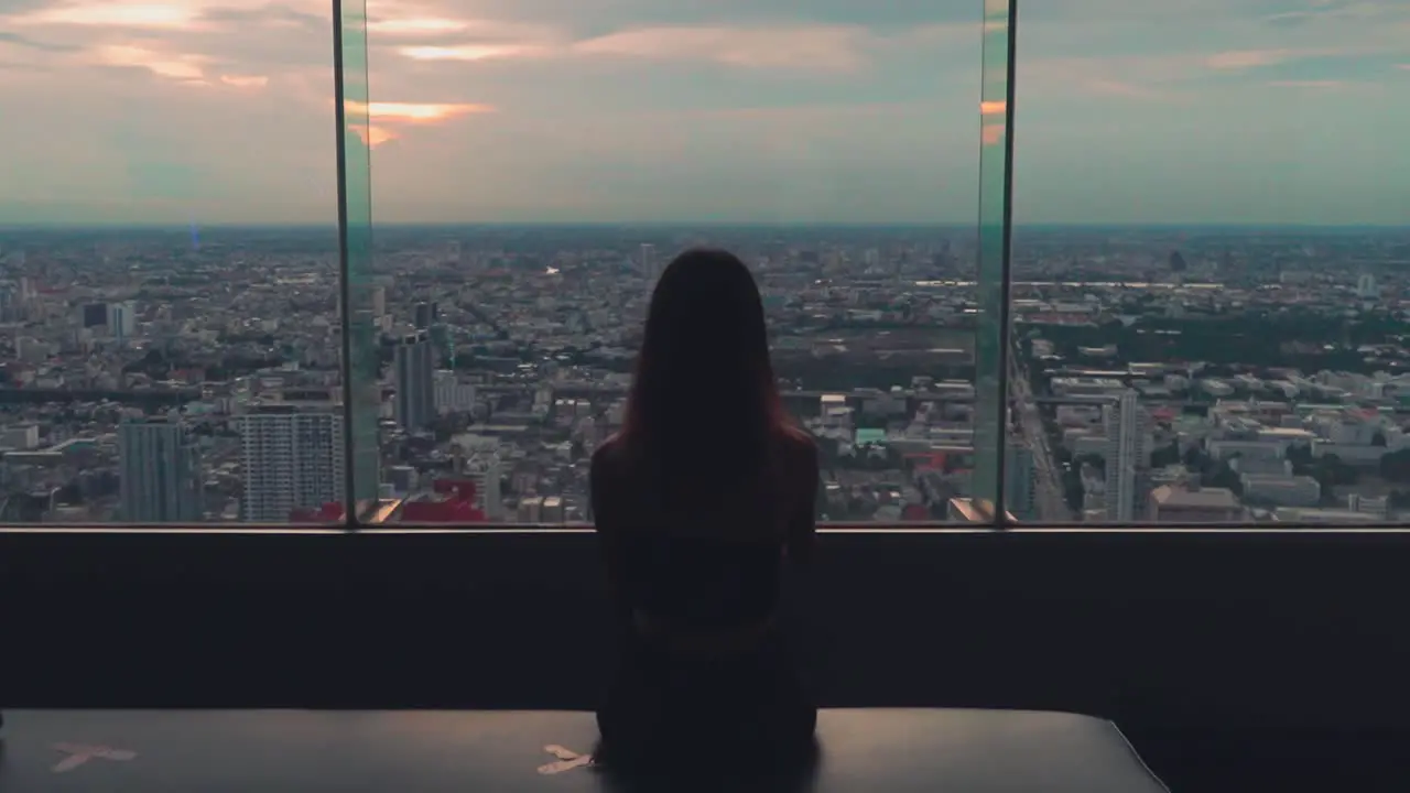 Girl sits and looks at Bangkok view on Baiyoke tower rooftop at sunset