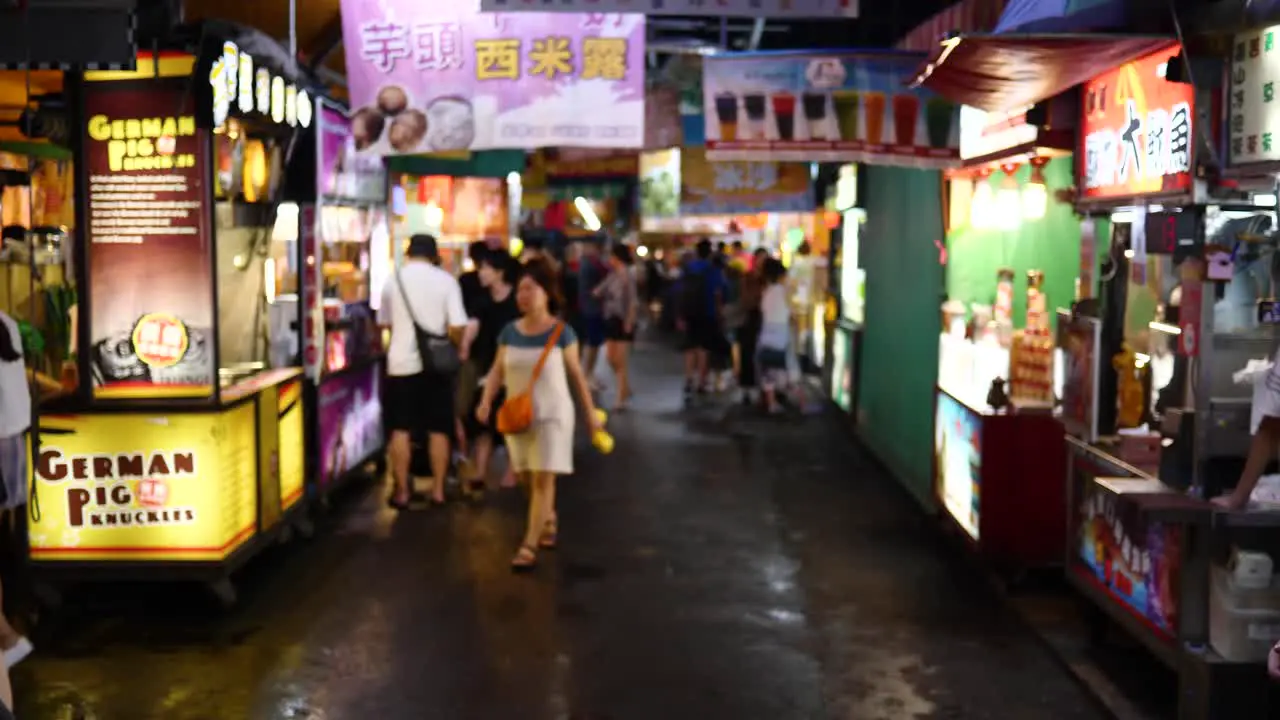 Night market food stalls and young Taiwanese customers walking past at night after a rain shower