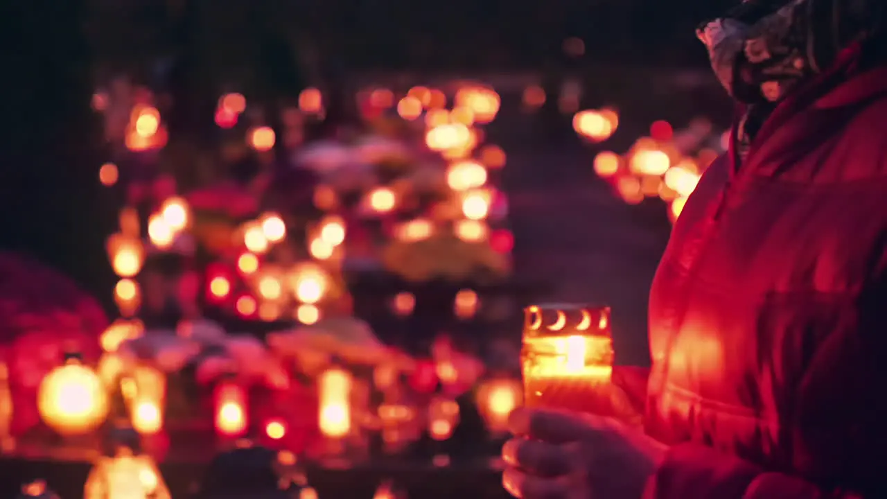 Woman holding burning candle walking through graveyard at night candles are shining in the dark