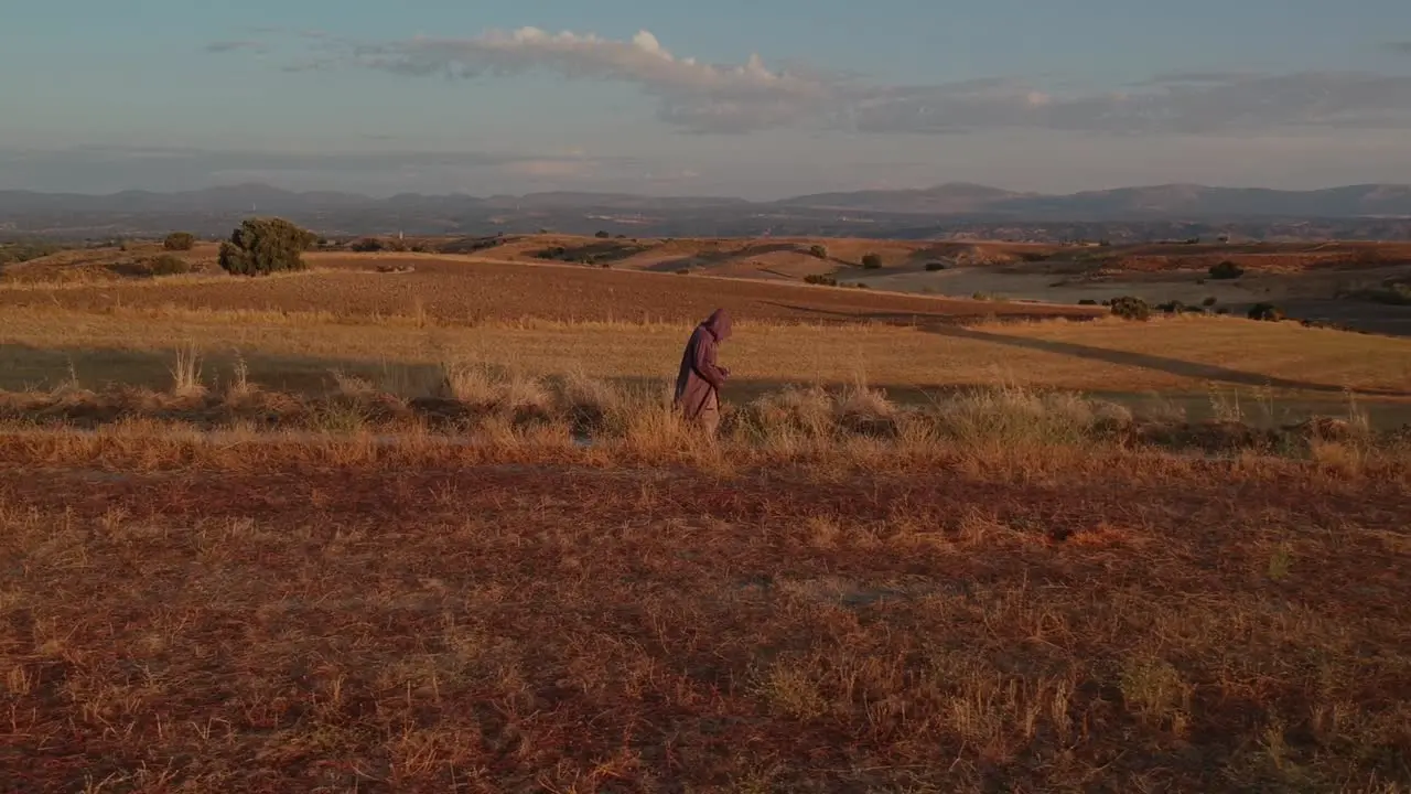 A profile shot following a monk walking towards right on a brown fields