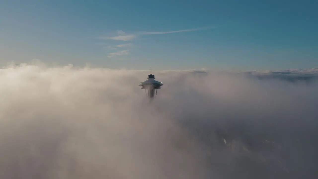 Aerial orbit around iconic city building breaking the dense layer of fog