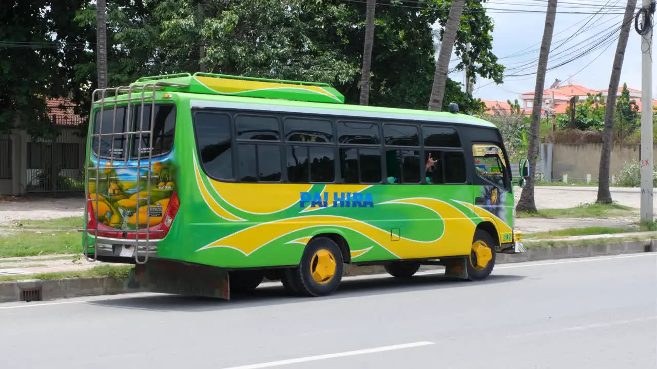 Cool funky modified bright green and yellow district bus transportation with person waving through window parked on street in capital city of East Timor Southeast Asia