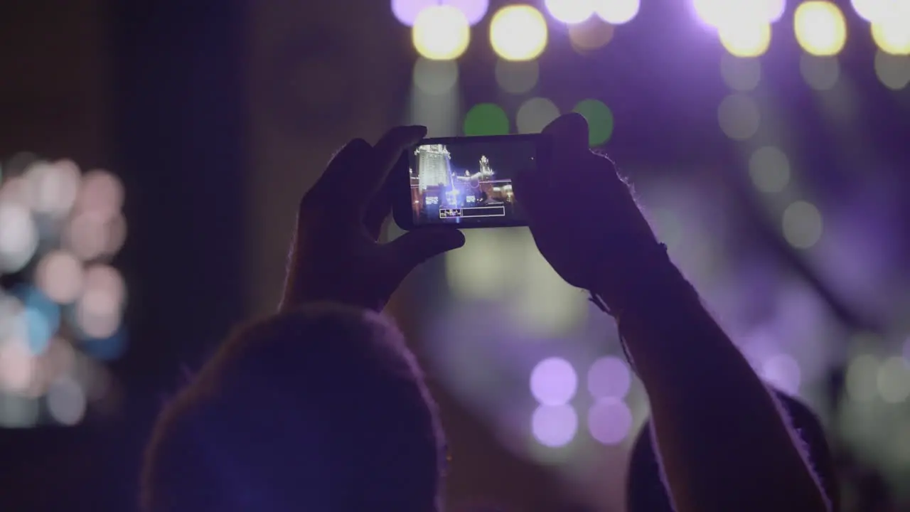 Spectator man makes a panoramic photo of stage with spotlights via smartphone at outdoor music concert