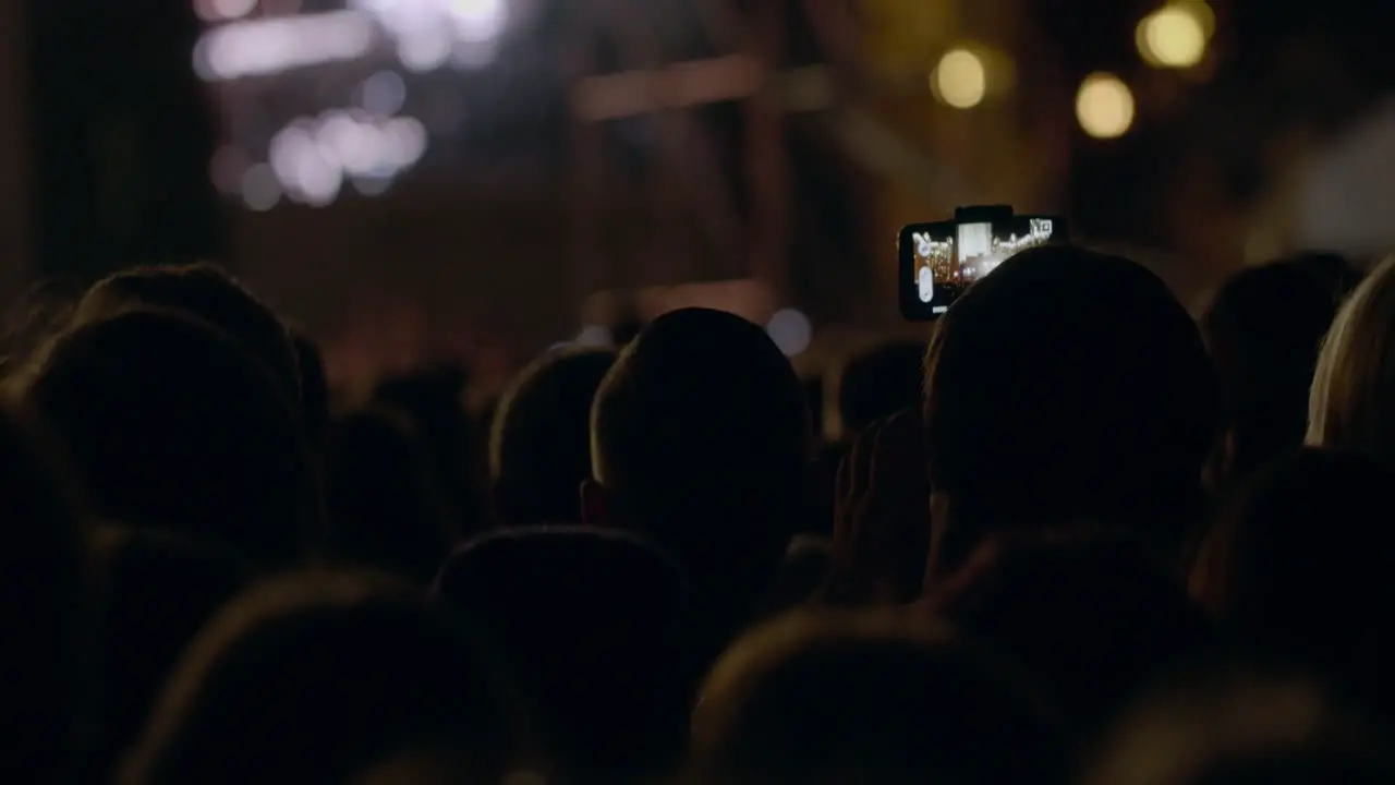 View from behind of hands hold camera with digital display among people at rave party with light