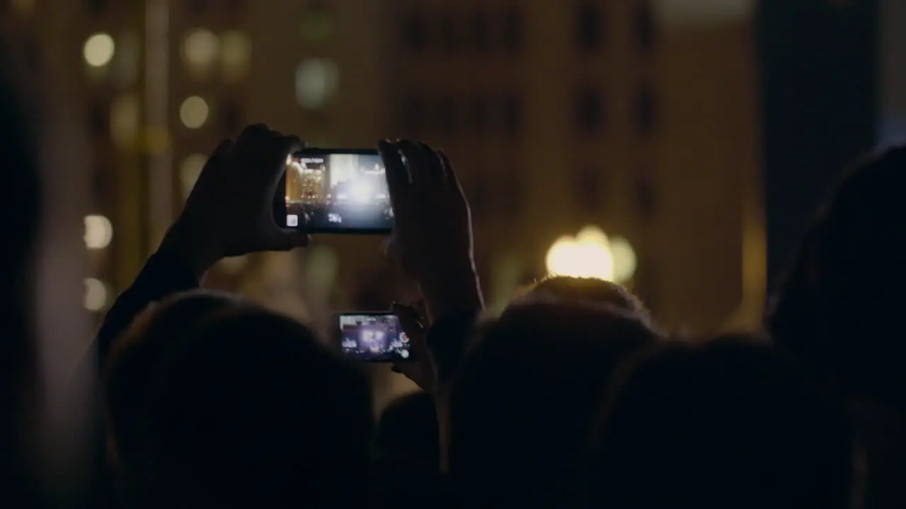 View from behind of hands hold smartphone among people at rave party with light