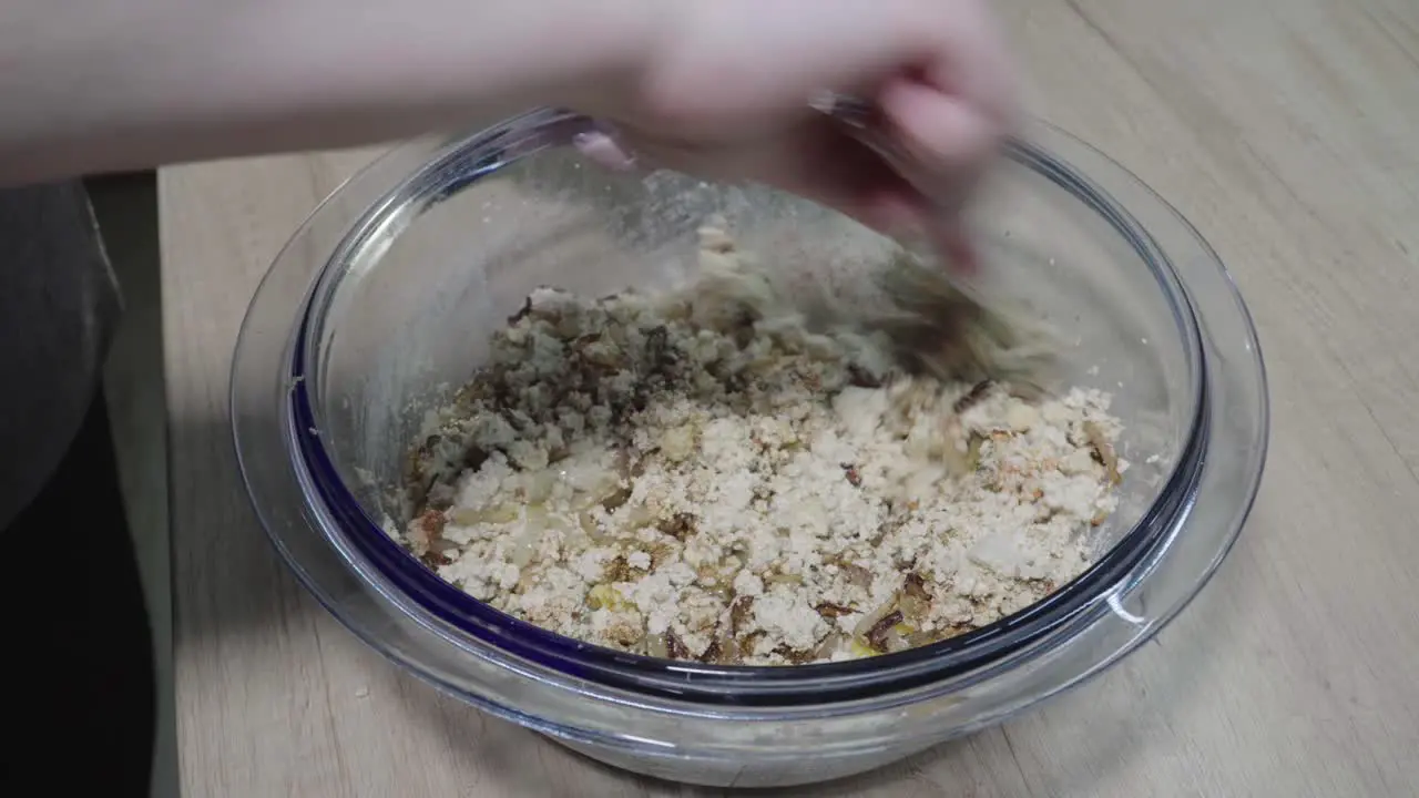 woman mixes crumpled tofu with spices and egg with a fork