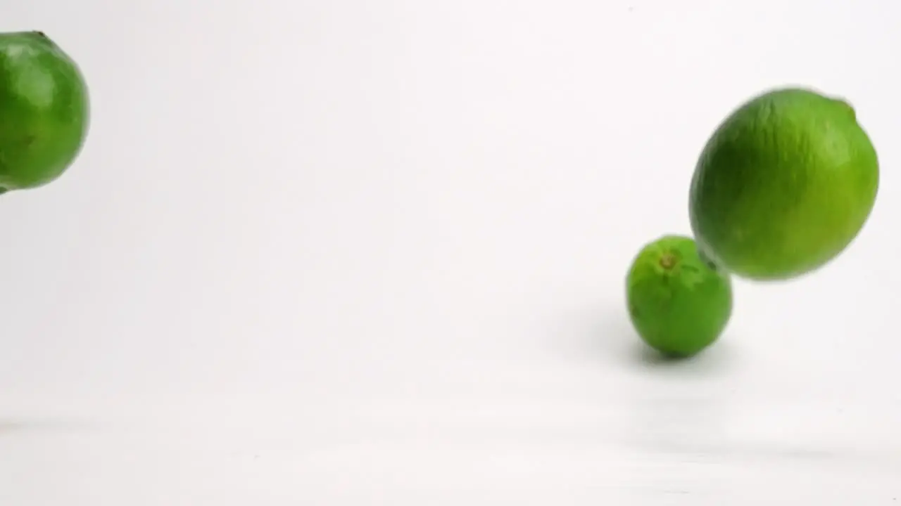 Bright green whole limes bouncing in slow motion onto white table top