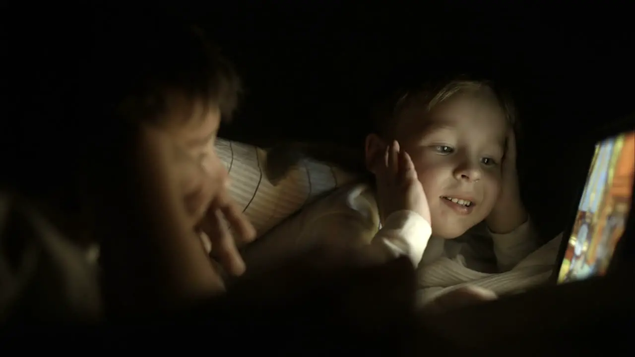 Two boys lying in bed at night and using pad