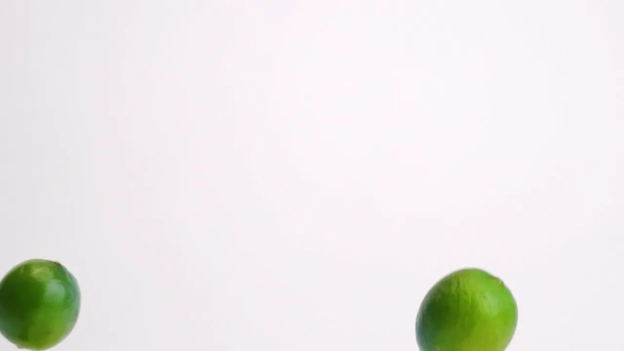 Whole green citrus limes raining down on white table backdrop in slow motion