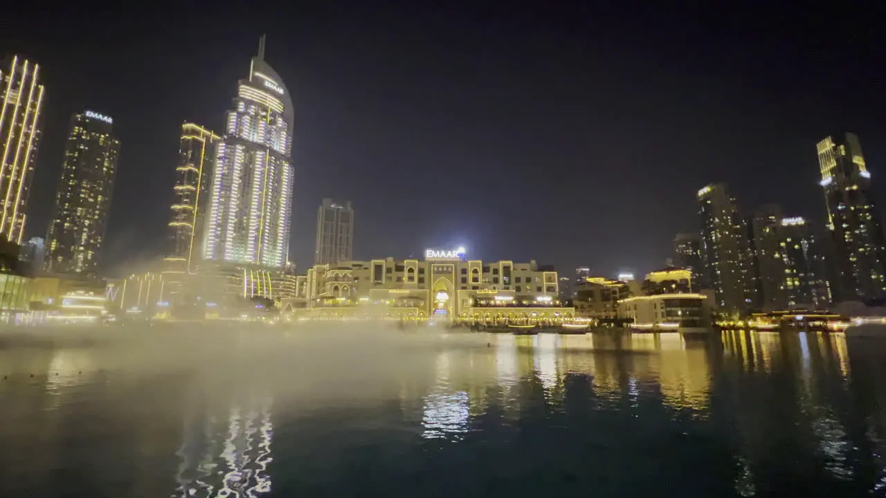 Smoke on the water in the Dubai fountain seen at night with luxurious restaurants in the background