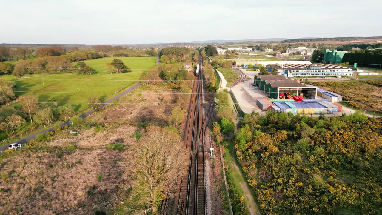 Train retreating into distance on a track with countryside on one side and warehousing and industrial estate on the other