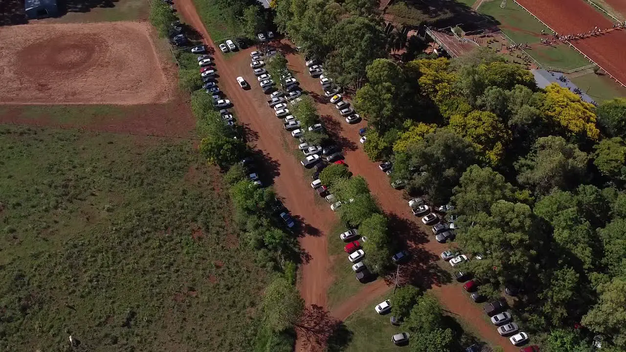 Drone orbit over car park in wooded area and surrounding fields cars drive past