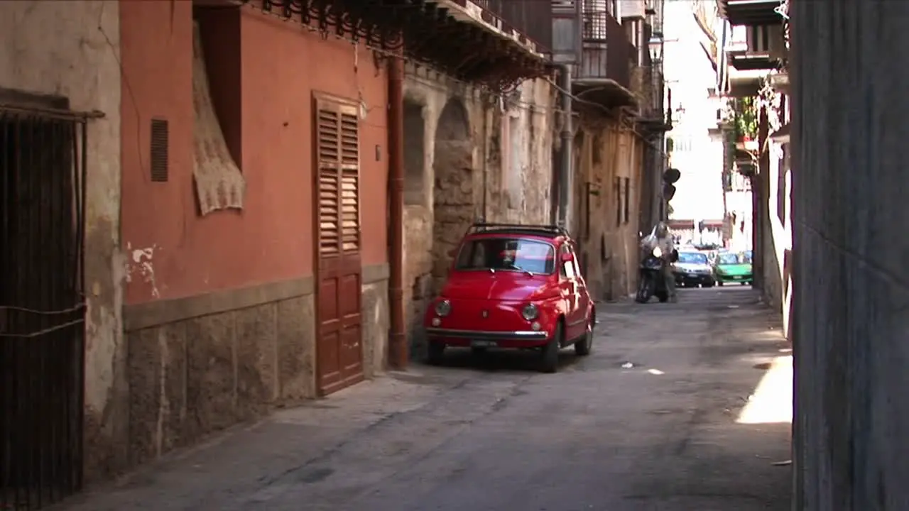 Cars parked along stone buildings in a tightly spaced alley Palermo Italy