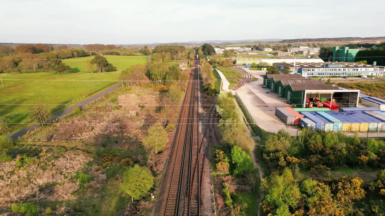 Train approaching and passing under drone shot on a track with countryside on one side and warehousing and industrial estate on the other