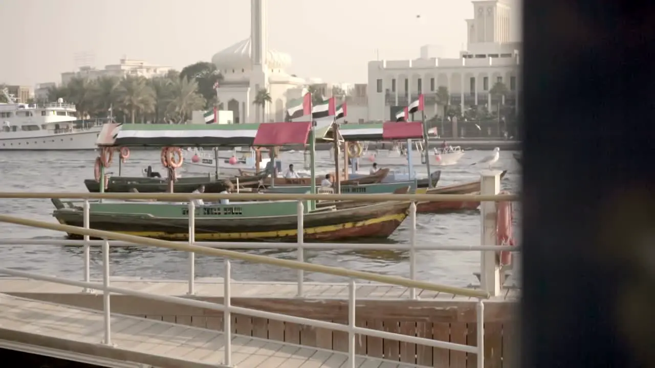 Wooden boats with Emirati flag idling in the Dubai Creek while other boats pass by in the background