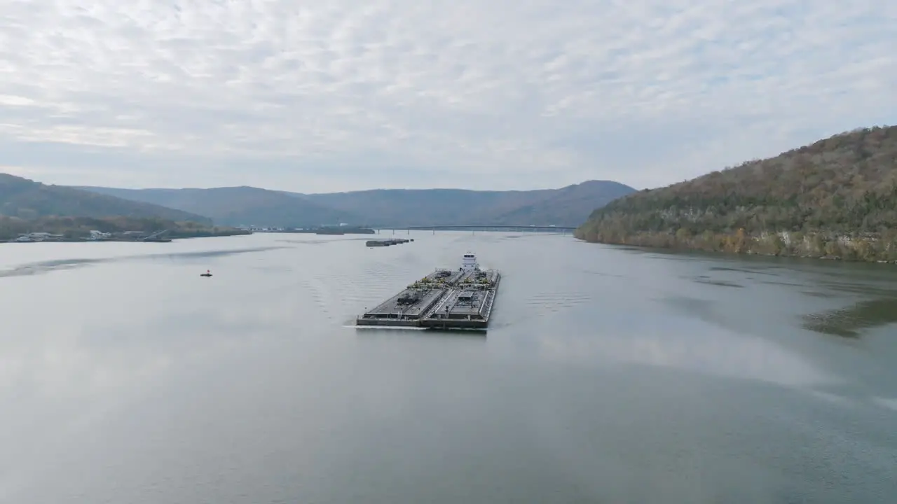 Aerial footage rotating around a pusher boat pushing a barge on Nickajack Lake with the morning sun peeking through the clouds