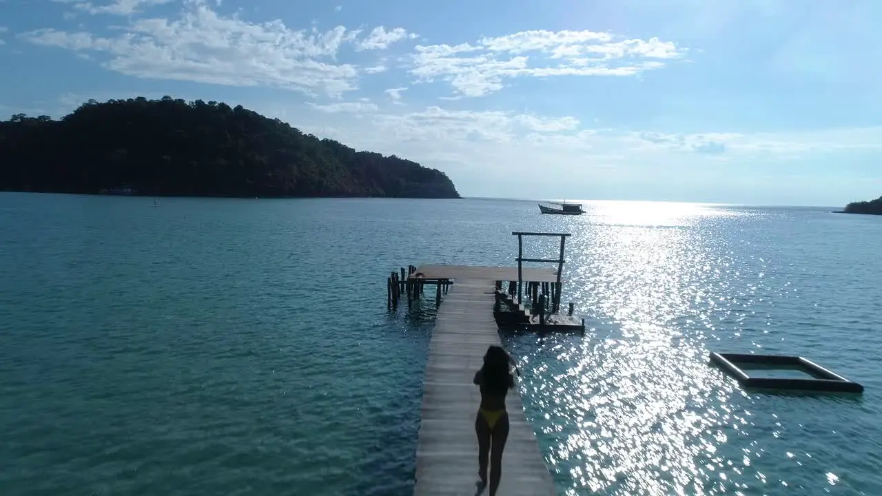 Fit Asian girl walking on a pier in the ocean on a tropical island koh kood thailand