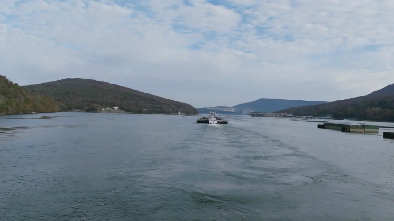 Aerial footage flying behind and then over a pusher boat moving large industrial barges on the Tennessee River in the morning in Autumn in Tennessee