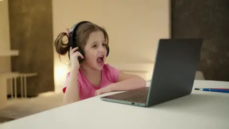 Pretty girl in headphones sit at home listen music on laptop playing computer game